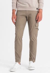 Pantaloni cargo slim-fit khaki con più tasche laterali, una texture morbida, abbinati a sneakers bianche per un look casual.