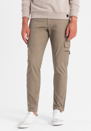 Pantalones cargo ajustados color caqui con múltiples bolsillos laterales, una textura suave y combinados con zapatillas blancas para un look casual.