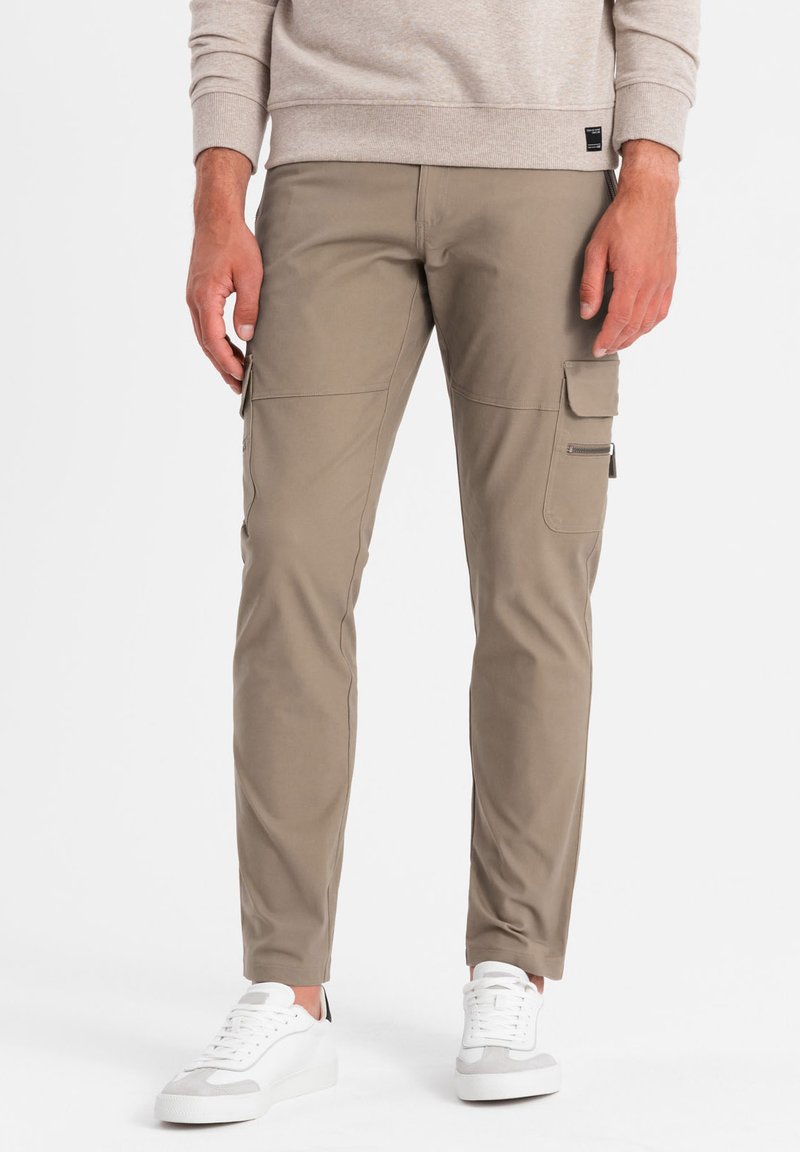 Pantaloni cargo slim-fit khaki con più tasche laterali, una texture morbida, abbinati a sneakers bianche per un look casual.