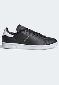 Schwarze Ledersneaker mit weißem Fersenakzent, mit durchbrochenen Details, schwarzen Schnürsenkeln und goldenem "STAN SMITH"-Logo an der Seite.