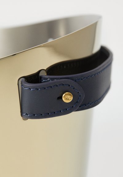 Metallic guldhink med en böjd topp. Utrustad med ett marinblått läderrem med guldfärgad hårdvara och detaljerad sömnad. Slät yta.