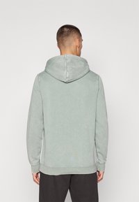 Light green sweatshirt with a hood, long sleeves, and ribbed cuffs. Soft texture and a relaxed fit. Minimalistic design with no visible logos.