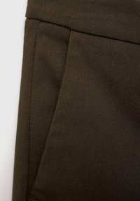 Tessuto verde scuro con una consistenza liscia e una leggera lucentezza, caratterizzato da una tasca laterale e dettagli di cucitura ordinati.