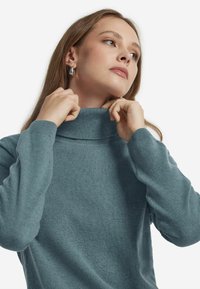 Hellblaue Rollkragenpullover aus einem weichen, strukturierten Stoff mit langen Ärmeln. Der Kragen ist umgeschlagen und schafft ein enges Halsdetail.