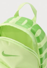 Žalios spalvos nailoninė kuprinė su užtrauktuku, viršutine rankena ir dideliu, persidengiančiu, skaidriu logotipu priekyje.