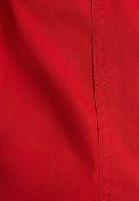 Tela roja con una fina textura diagonal y costuras visibles. Superficie suave con un ligero brillo, que enfatiza su color vibrante.