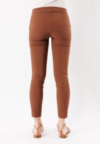 Pantaloni marroni aderenti con vita alta, texture liscia e design elegante. Taglio alla caviglia con dettagli di cucitura minimi.