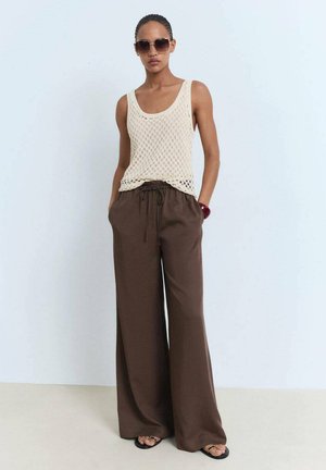 Beige knitted tank top with large mesh pattern, paired with brown wide-leg pants with elastic waist, and black sandals. Dark sunglasses complement the outfit.