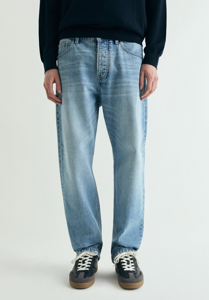 Lyseblå denim jeans med løs pasform, som har et klassisk design med fem lommer og en falmet tekstur. Kombineret med sorte sneakers og hvide snørebånd.