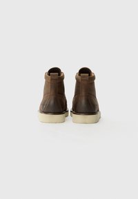 Botas negras de cuero con textura suave, que presentan una suela de goma blanca en contraste y mínimos detalles de costura en la parte trasera.