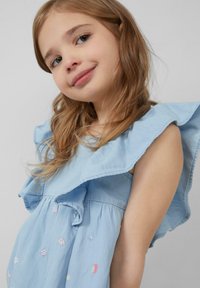 Light blue cotton dress with ruffled shoulders, embroidered floral details, and a gathered waist. Soft texture and relaxed fit.