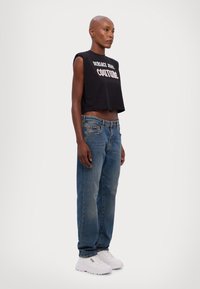 Fekete cropped tank top, amit a "Versace Jean Couture" felirat díszít, világoskék egyenes lábú farmernadrággal és fehér, vastag talpú tornacipővel párosítva.