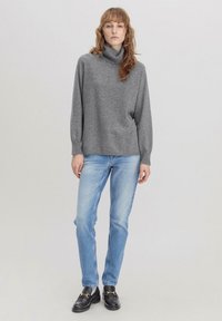 Grijze coltruibroek met lange mouwen, gecombineerd met lichtblauwe rechte jeans en zwarte instappers met gouden accenten.