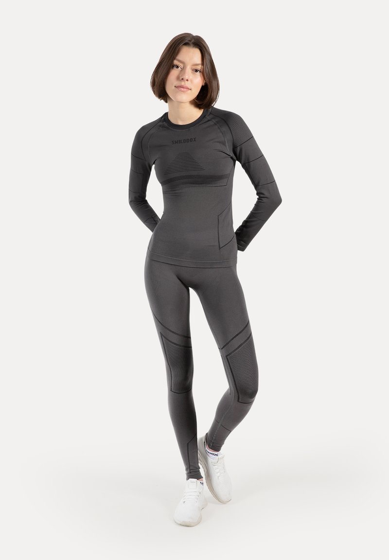 Sort atletisk sæt bestående af en langærmet top og leggings lavet af strækbart stof med teksturerede detaljer og en tætsiddende pasform.