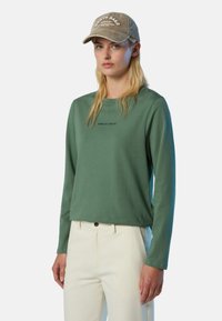 Langärmliger grüner Baumwollpullover mit Rundhalsausschnitt und gesticktem "NORTH SAILS"-Logo auf der Brust, kombiniert mit cremefarbenen Hosen.