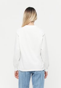 Hvid langærmet sweatshirt med rund hals, tykke manchetter og en afslappet pasform, parret med lyseblå vertikalt stribede jeans.