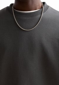 Gros plan d'une personne portant un sweat-shirt à col rond gris foncé et un collier en chaîne argentée.