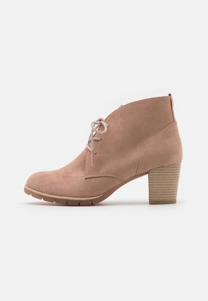 Beżowy zamszowy botek za kostkę z przodu na sznurowadła i złożonym blokowym obcasem na jednolitym białym tle.