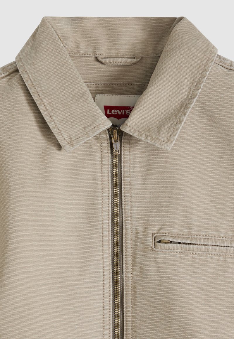 Beige Levi's Jacke mit spitzem Kragen, Frontreißverschluss und Reißverschlusstasche auf der rechten Brustseite.