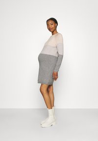 Nėštumo suknelė su ilgomis rankovėmis, spalvų derinys: smėlio, šviesiai pilkos ir tamsiai pilkos. Modelis vilki baltus ankle batus. Minkšta mezginio tekstūra.