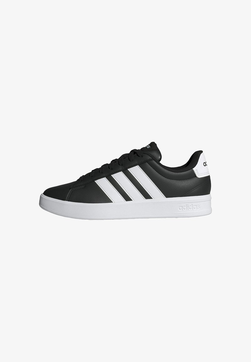 Baskets basses noires Adidas avec trois bandes blanches, semelle blanche et languette de talon marquée, présentées de profil sur fond blanc.