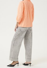  ferskenfarvet bluse med zigzag-mønster og puffede ærmer, kombineret med grå høj talje, brede bukser og sorte mulehæle.