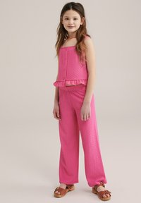 Rúžový dvojdielny outfit so štruktúrovaným, bezramienkovým topom s volánovým lemom a zodpovedajúcimi širokými nohavicami. Hnedé drevené klobúky s prackami.