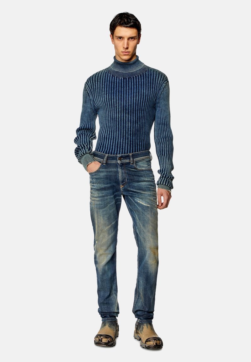 Gebreide turtleneck trui in donkerblauw met geribbelde textuur, gecombineerd met vervaagde blauwe jeans en bruine schoenen met een gestructureerd ontwerp.