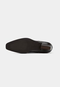 Sola de sapato de salto alto em couro preto com uma forma suave e arredondada. Apresenta uma sola texturizada para aderência e um discreto detalhe castanho no calcanhar.