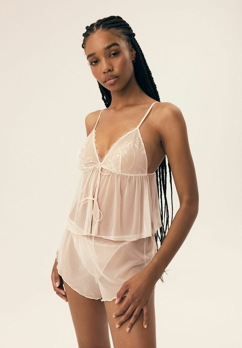 Przezroczysty, jasnoróżowy zestaw bielizny składający się z warstwowej bluzeczki na ramiączkach z haftem, regulowanymi ramiączkami oraz dopasowanych szortów z falbaniastymi krawędziami.