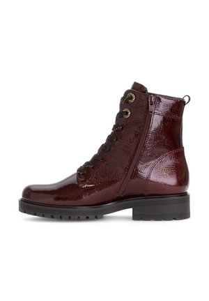 Botte cheville laquée rouge foncé avec des lacets noirs, fermeture éclair latérale, œillets dorés et épaisse semelle en caoutchouc noir.