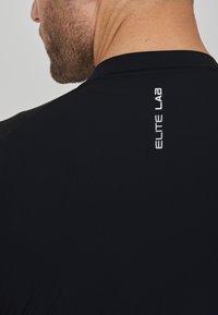 Schwarzes Sportshirt mit figurnaher Passform, ausgestattet mit einem reflektierenden "ELITE LAB"-Logo nahe dem Rückenausschnitt und einem glatten, leichten Stoff.
