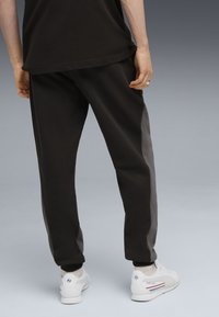 Zwarte sweatpants met een grijze zijpaneel, met een ontspannen pasvorm en elastische boorden, gecombineerd met witte sneakers. Glad textuur van de stof.