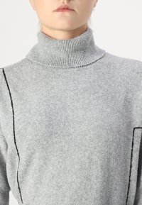 Siv pulover s turtleneck ovratnikom, izdelan iz mehkega pletenega materiala, z ribastim ovratnikom in kontrastnim črnim šivom ob straneh.