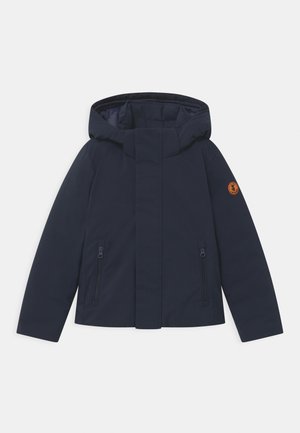 Tmavě modrá prošívaná bunda s kapucí, přední zapínání na zip kryté légou, dvě kapsy na zip a oranžová kulatá nášivka na levém rukávu.