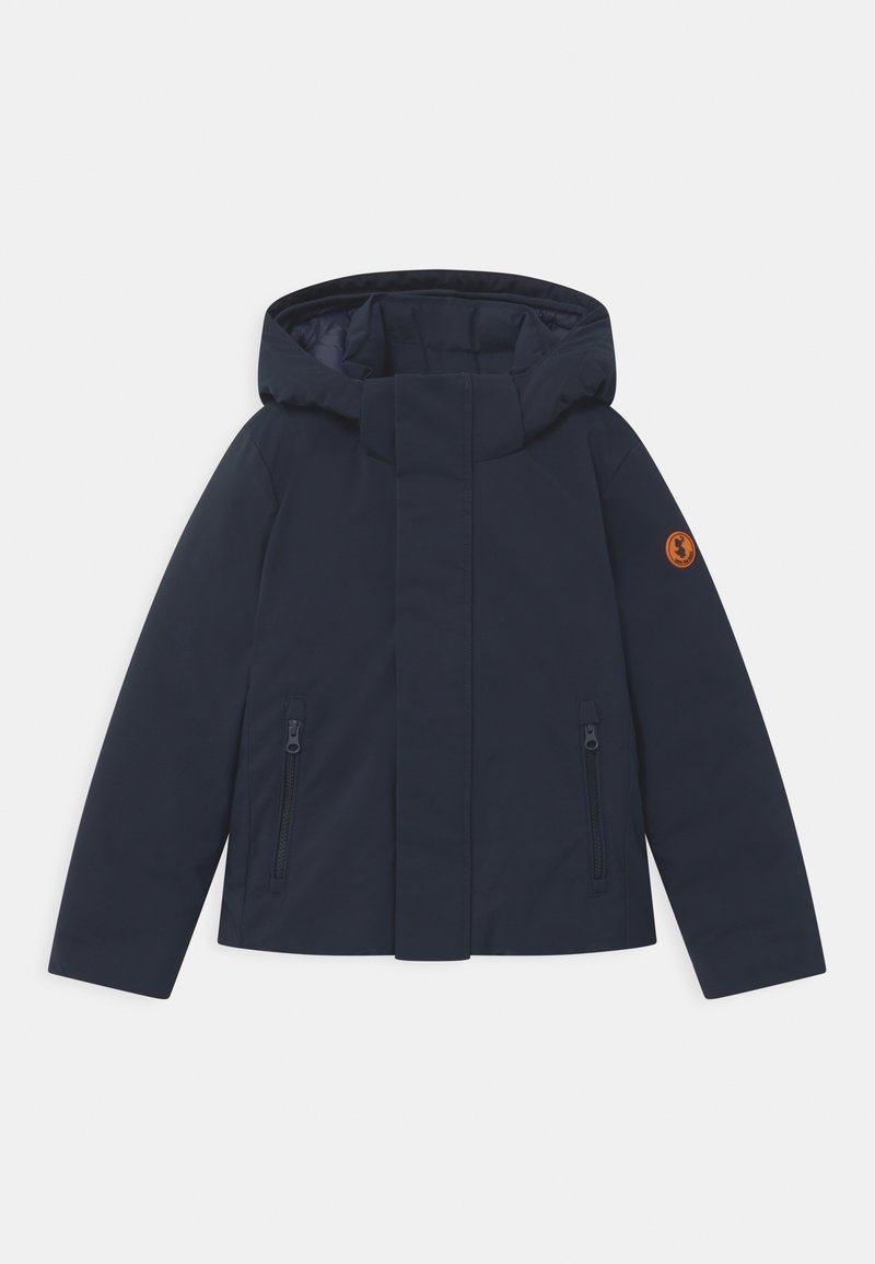 Veste matelassée bleu marine avec capuche, fermeture éclair frontale couverte par un rabat, deux poches zippées, et patch circulaire orange sur la manche gauche.