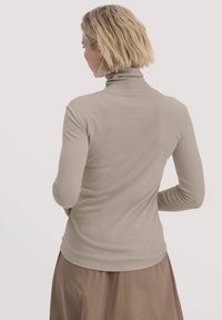 Beige Langarm-Turtleneck-Oberteil mit taillierter Passform und glatter Textur, getragen mit einem braunen Rock, von hinten gezeigt.