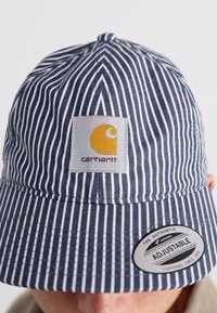 Blue and white striped bucket hat featuring a Carhartt logo patch and an adjustable strap with a round tag on the brim.