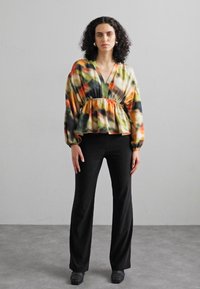 Bluză peplum multicoloră, confecționată dintr-un material ușor, cu decolteu adânc în V și mâneci lungi, asortată cu pantaloni sunați negri.