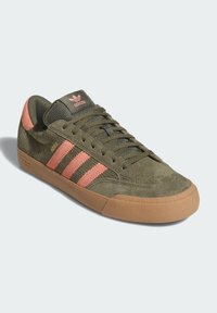 Αθλητικό παπούτσι από σουέτ σε ελιά πράσινο με ροζ σχέδιο τριών λωρίδων, υφασμάτινη γλώσσα με ανάγλυφη υφή και σόλα από καουτσούκ χρώματος καραμέλας. Διαθέτει ενισχυμένη μύτη και κεντημένο λογότυπο.