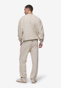 Felpa beige in cotone con spalle scese, vestibilità comoda e polsi a costine, abbinata a pantaloni della tuta coordinati e sneakers bianche.