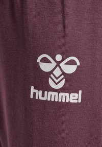 Bordeaux sportbroek met witte bedrukte logo en ontwerp. Materiaal is textuurachtig met fijne ribbels en een gladde afwerking.