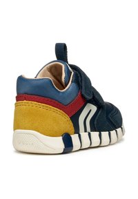 Zapatilla de color azul marino con acentos rojos y amarillos. Hecha de ante y materiales sintéticos, con una suela flexible y una correa de velcro.