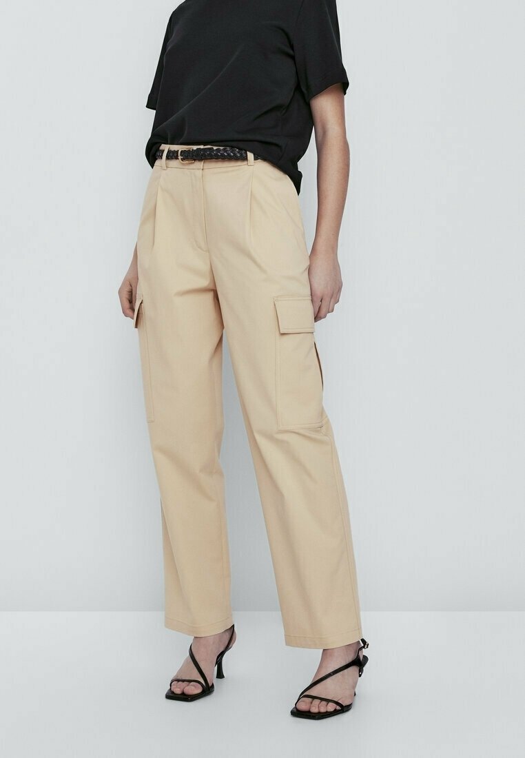 Beige cargobroek met een losse pasvorm, twee zijzakken en een hoge taille. Gepaard met een zwart T-shirt met korte mouwen en zwarte strapsandalen.