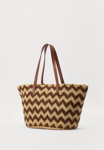 Tkanina torba s rjavim zigzag vzorom in dvema dolgima rjavima usnjenima ročajema na enobarvni svetli podlagi.