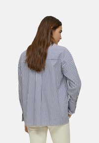 Camicia a righe blu navy e bianca con vestibilità ampia, maniche lunghe e colletto tradizionale. Presenta un pettorina posteriore e polsini con bottoni.