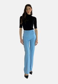 Zwart kortemouw turtleneck top gecombineerd met lichtblauwe hoge taille flared broek en zwarte puntige hielen. Glad materiaal, getailleerde pasvorm.