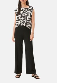 Sort og hvid top med abstrakt mønster, kortærmet, parret med højderede sorte vidde bukser og sorte flade sandaler.