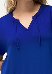 Korte mouwen blauwe top met een V-hals. Gemaakt van een zachte stof. Heeft een trekkoord detail bij de halslijn.