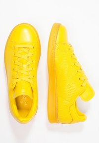 Gula sneakers gjorda av slätt och perforerat läder, med runda tår, snörning och en texturerad gummisula.